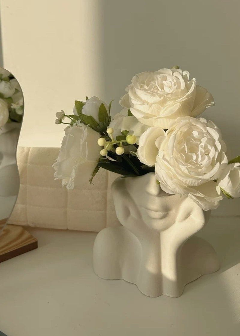 White ceramic vase with face design holding white flowers on a light background
